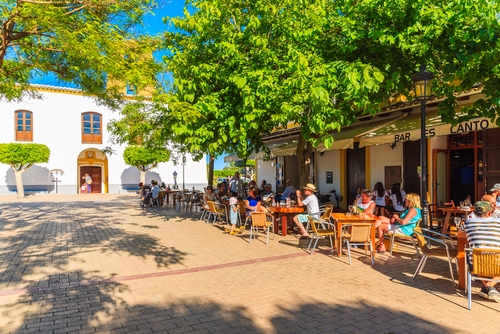 People sitting outdoors in restaurants on church square in Santa Getrudis village on Ibiza Island, Balearic Islands, Spain