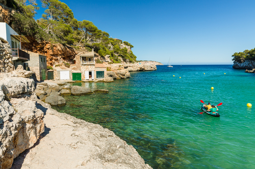 Two people with a kayak at Cala Llombards, a beautiful beach that is sheltered on either side by cliffs, Mallorca island, Balearic Islands, Spain