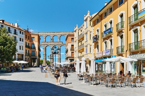 People walking near the Roman Aqueduct and the Azoguejo Sqaure cafes and restaurants at the ancient Spanish european city of Segovia, Castile and León, Spain