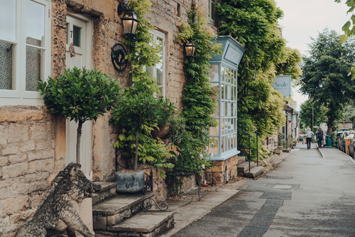 Row of houses on a main street in Stow-on-the-Wold, some local residents on the background. Stow a market town in Cotswolds, England, UK, built on Roman Fosse Way
