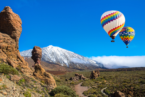Beautiful view of hot air balloons and the unique Roque Cinchado rock formation with the famous volcano Teide in the background on a Sunny day, Teide National Park, Tenerife island, The Canaries, Spain