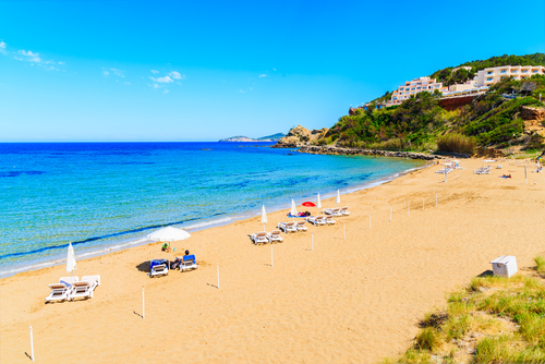 View of the beautiful sandy Es Figueral beach with its sunbeds and umbrellas, Ibiza island, Balearic Islands, Spain