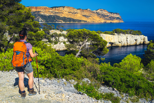 Sporty hiker woman with backpack enjoying the view with blue water bay from the hiking trail in Calanques National Park, Provence, France