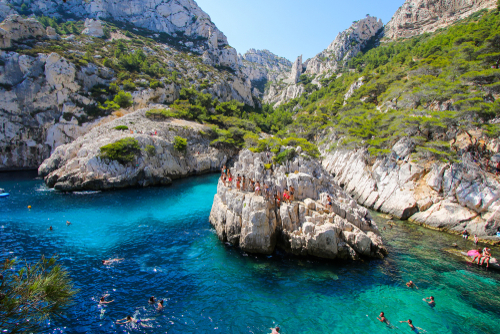 Small island in the center of the cove of Sugiton in the Calanques de Marseille National Park in the south of France - Tourists jumping in the turquoise waters of the Mediterranean Sea, Provence, France
