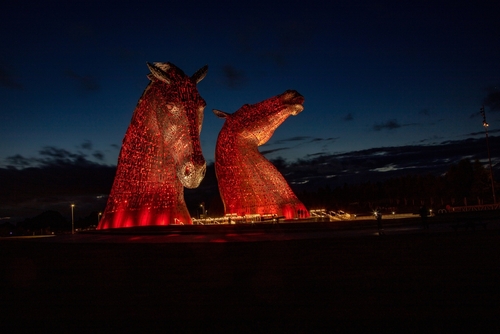 The Kelpies, a sculpture on the Helix Park. Illuminated in red against a night sky. Falkirk in Scotland, UK