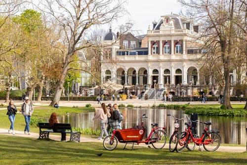 People walk and cycle in the famous Vondelpark with the Vondelpark Pavilion in the background, built by architect W. Hamer in Italian Renaissance style, Amsterdam, The Netherlands