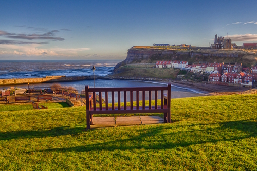 A wooden bench on a hillside facing the sea and the cliff at Whitby, North York Moors National Park, Yorkshire, England, UK
