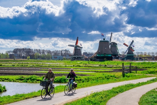 Famous windmills, warehouses and workshops at the Zaanse Schans Village in Zaandam near Amsterdam, The Netherlands, on a Sunny spring day with tourists riding on bikes