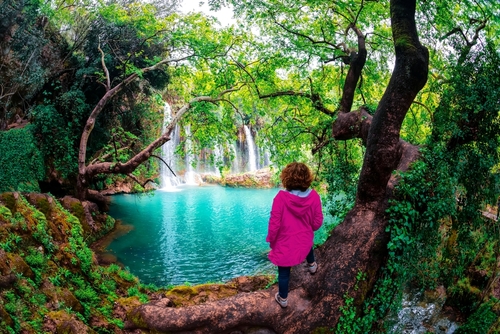 Girl overlooking the beautiful waterfalls over emerald water in deep green forest in Kursunlu Natural Park, Antalya, Turkey