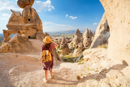Back view of young woman exploring valley with rock formations and fairy chimneys near Uchisar castle in Cappadocia, Turkey