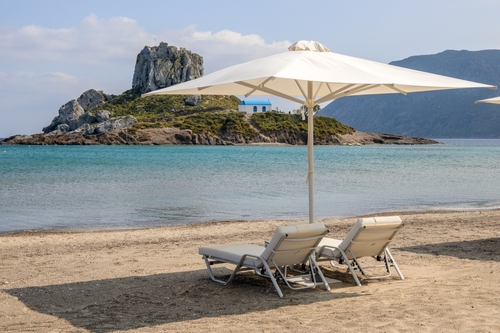 Sunbeds with umbrella on the sandy beach of Agios Stefanos with a lookout to the small Islet of Kastri, the Island of Kos, Dodecanse Islands, Greece