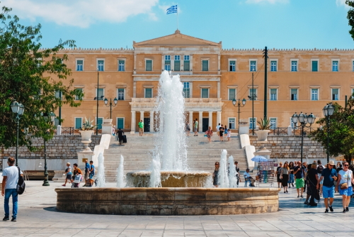 People walking around Syntagma Square with the fountain in the middle with the Old Royal Palace in the background, Athens, Greece