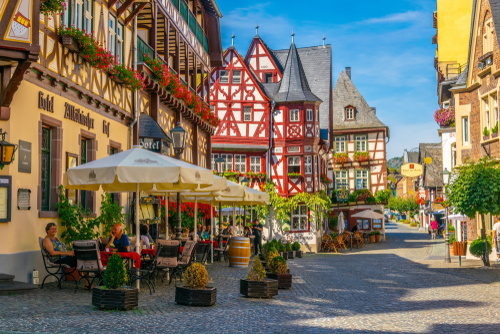 People sitting in a restaurant and colorful half-timbered houses around in the historical Old town center of Bacharach, Rhine Valley, Rhineland-Palatinate, Germany