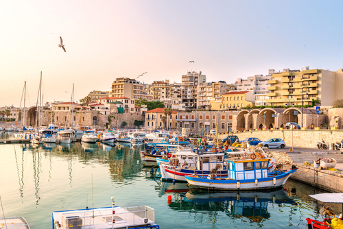 View to Heraklion in the early morning during Sunrise, the old port with traditional fishing boats and town with its ancient buildings at the background, Island of Create, Greece