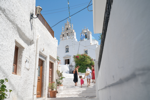Three woman with small child walk up steps on path between white village buildings towards church in the village of Filoti, Naxos Island, Cyclades Islands, Greece