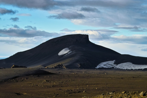Sand dune shaped hill with spots of snow in rocky volcanic area around the trail to the top of Hekla volcano, Landmannalaugar Reservation, Iceland