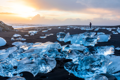Diamond Beach in Iceland with blue icebergs melting on the black sand and ice glistening with sunrise sun light, tourist looking at beautiful arctic nature scenery, Icelandic South coast, Jokulsarlon