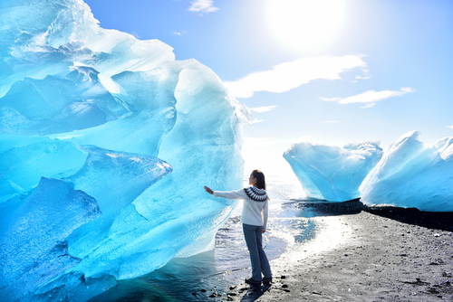 Woman touching an iceberg, Iceland amazing landscape at Iceberg beach. Tourist by icebergs on Ice beach, Breidamerkursandur aka Diamond Beach by Jokulsarlon glacial lagoon