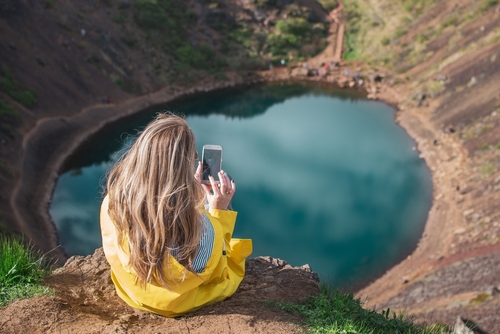Woman in a yellow coat looking over the Kerid Volcanic Crater in the Golden Circle, Iceland