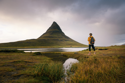 Young hiker with a backpack looks at the Kirkjufell mountain in Iceland. This 463 m high mountain is located on the north coast of Iceland's Snaefellsnes peninsula