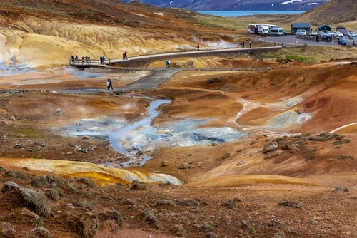 Seltun Geothermal Area in Krysuvik with steaming hot springs, yellow and orange sulphur hills, people walking on boardwalks, Iceland