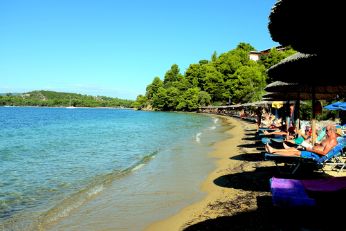 Holidaymakers relaxing in the September sunhsine on Maratha beach and its facilities with Koukounaries beach in the background on the Island of Skiathos, Sporades Islands, Greece