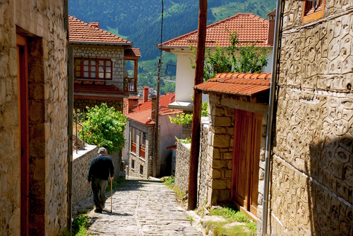 An old man walking with a cain down a cobbled stone alley in the streets of Metsovo a town in Epirus on the mountains of Pindus at northern Greece