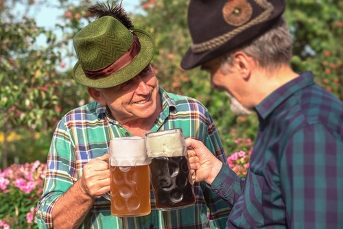 Men with beer mugs with Bavarian beer in Tyrolean hats with feathers celebrating beer festival outdoor among the trees in Germany. Happy old Germans people. October Munich holiday on a Sunny day, Bavaria, Germany