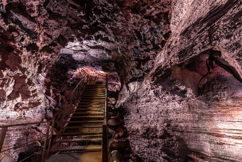 Purple illuminated rock structures and a staircase in the Raufarholshellir lava tunnels near Reykjavik, Iceland