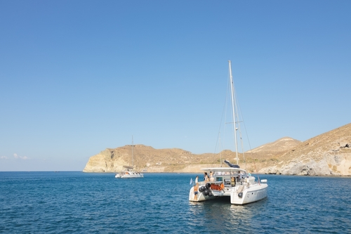 Tourists enjoy a catamaran boat excursion on the Aegean Sea along the coast of the Greek Island Santorini, Cyclades Islands, Greece