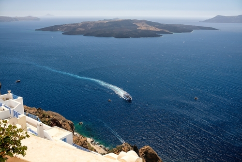 View of a small ferry boat approaching the old harbor and the volcano of Santorini in the background, Cyclades Islands, Greece
