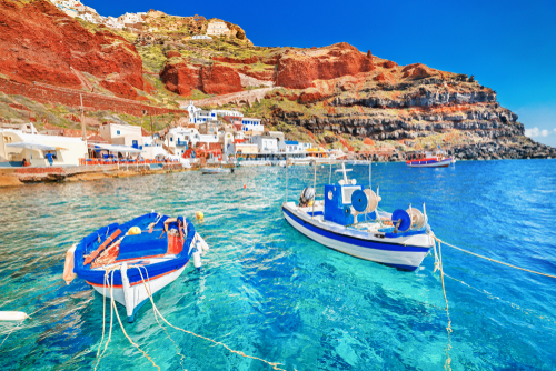 Breathtaking view of two fishing boats anchored to quay in fascinating blue water at the amazing old port in Oia village on Santorini Island in the Aegean sea, Greece