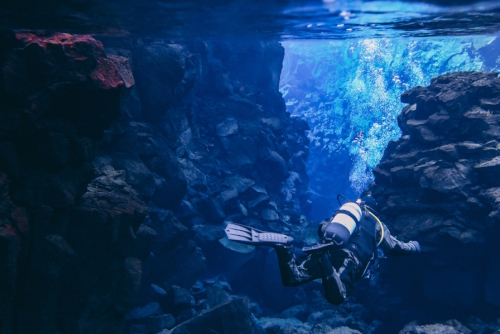 Divers scuba diving between two tectonic plates in crystal clear water in the Silfra fissure located in Thingvellir National Park, Iceland. Great visibility of volcanic rock formations