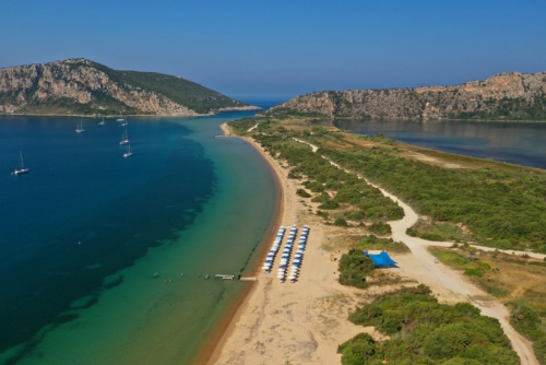Aerial view of the iconic sandy beach of Divari (chrysi akti) and its facilities, with emerald sea near island of Sfaktiria in bay of Navarino, Messinia, Gialova, Peloponnese, Greece