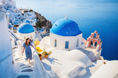 Beautiful girl on Summer vacation enjoying breathtaking view of blue-domed church in Oia village on the Island of Santorini, Greece