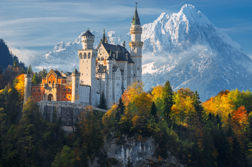 The famous Neuschwanstein Castle in the background of snowy Bavarian Alps and trees with yellow and green leaves in Bavaria, Germany