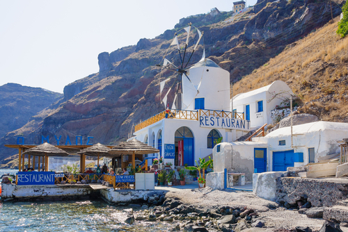Aegean Sea coast scene with restaurant and windmill on the Island of Therasia next to the Island of Santorini, Cyclades Islands, Greece