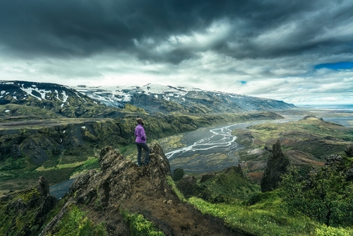 Dramatic volcanic landscape of Valahnukur trail and hiker woman standing in Thorsmork valley, Landmannalaugar Reservation, Iceland. Moody sky in Summer