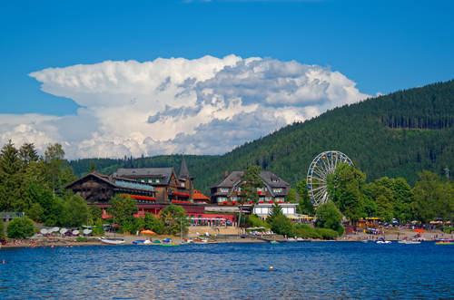 Beautiful view on the promenade, traditional houses and Ferris Wheel over the lake Titisee against amazing cloudy sky in the Black Forest, Baden-Württemberg, Germany