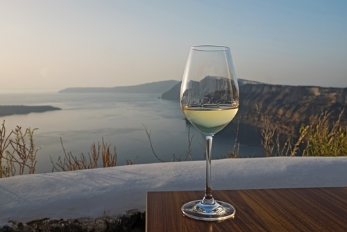 Glass of a white wine standing on the table with a view to Santorini caldera, Santorini Island, Cyclades Islands, Greece