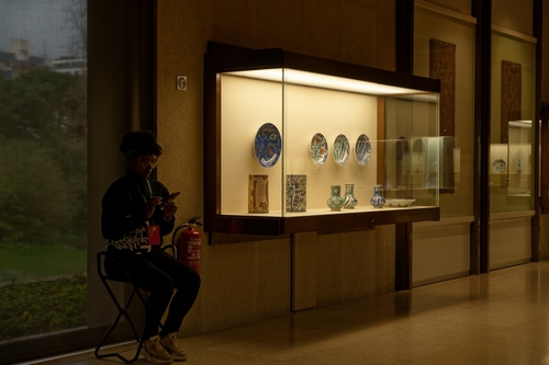 Museum attendant sits beside a display of intricate ceramics at the Calouste Gulbenkian museum in Lisbon, Portugal