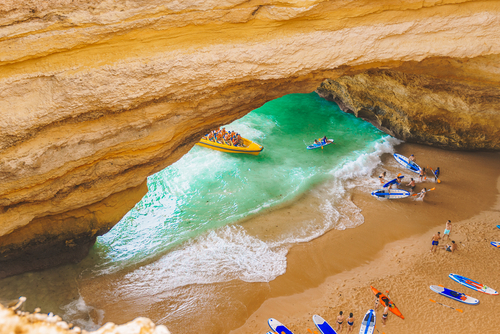 Benagil cave in Carvoeiro, Algarve, Portugal. Tourists swimming on paddle boards for SUP, kayak, motor boats to Praia de Benagil. learn about the Benagil Cave and the beautiful beaches in thetjoy.com