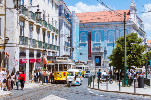 A yellow old tram rides along the Largo do Chiado. Church Nossa Senhora do Loreto and incidental people in background, Lisbon, Portugal