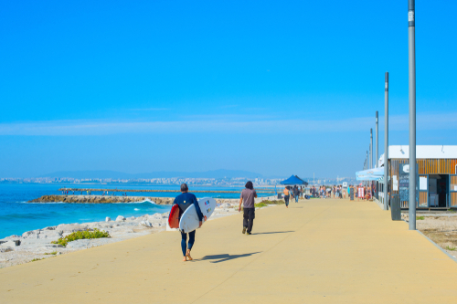People walking by seaside promenade in the sunny summer day, Costa de Caparica, Lisbon, Portugal