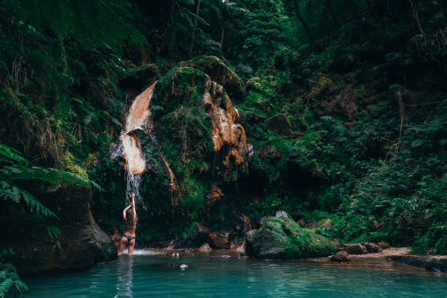 young lady under hot waterfall in Sao Miguel Island, Azores Islands, Portugal. Caldeira Velha park with hot springs, like in the jungle