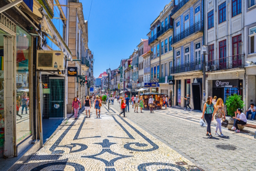 People walking down Rua de Santa Catarina cobblestone pedestrian street with colorful buildings and houses in historical city centre in sunny summer day, Porto, Portugal