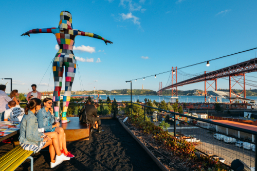 View of 25th of April bridge with people sitting on the bar terrace at LX Factory in Alcantara during the sunset in Lisbon city, Portugal